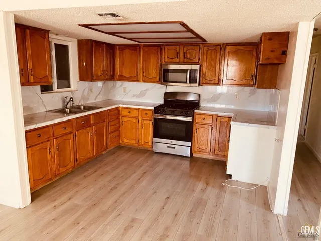 a kitchen with granite countertop a stove top oven a sink dishwasher and a refrigerator with wooden floor