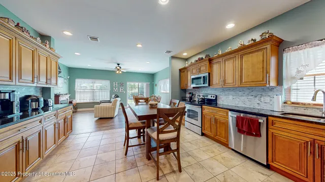 a kitchen with stainless steel appliances granite countertop a stove top oven a sink dishwasher a dining table and chairs with wooden cabinets