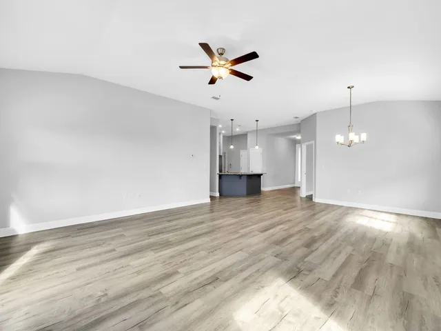 a view of an empty room with wooden floor and a ceiling fan