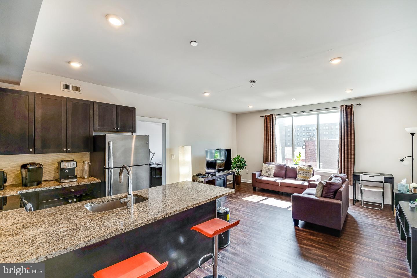 a living room with stainless steel appliances granite countertop a couch wooden floor and a refrigerator