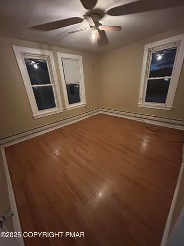 a view of an empty room with wooden floor and a ceiling fan