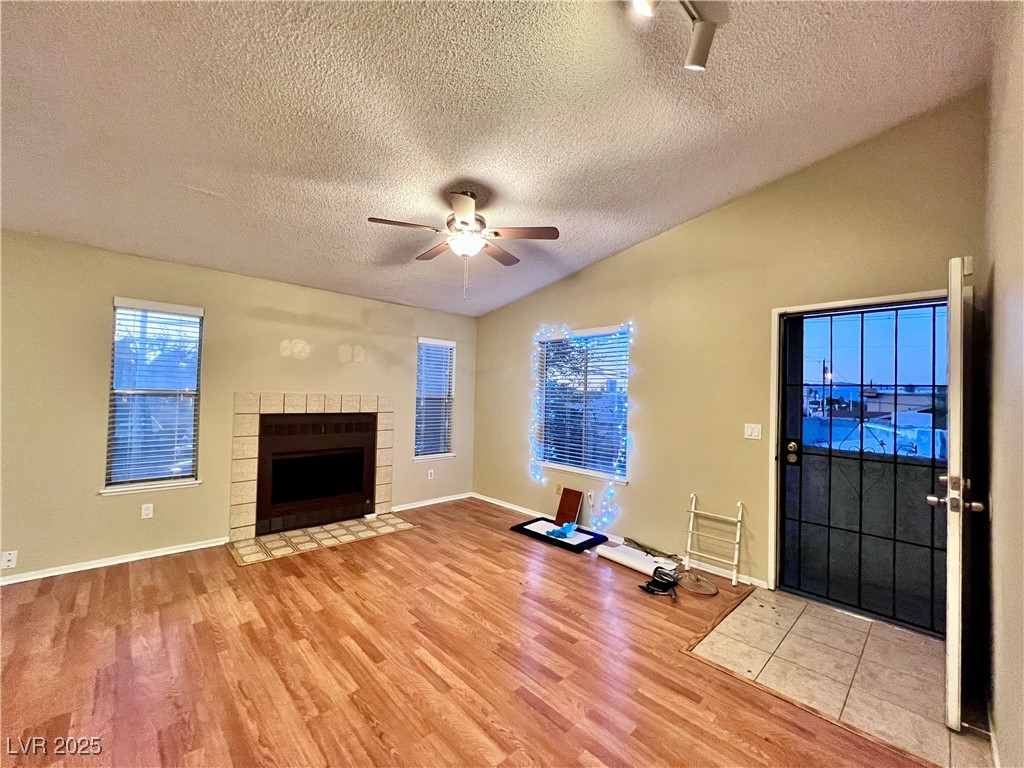 Unfurnished living room featuring light wood finished floors, a textured ceiling, a fireplace with flush hearth, vaulted ceiling, and ceiling fan