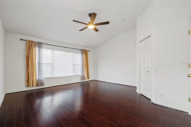 an empty room with wooden floor a ceiling fan and windows