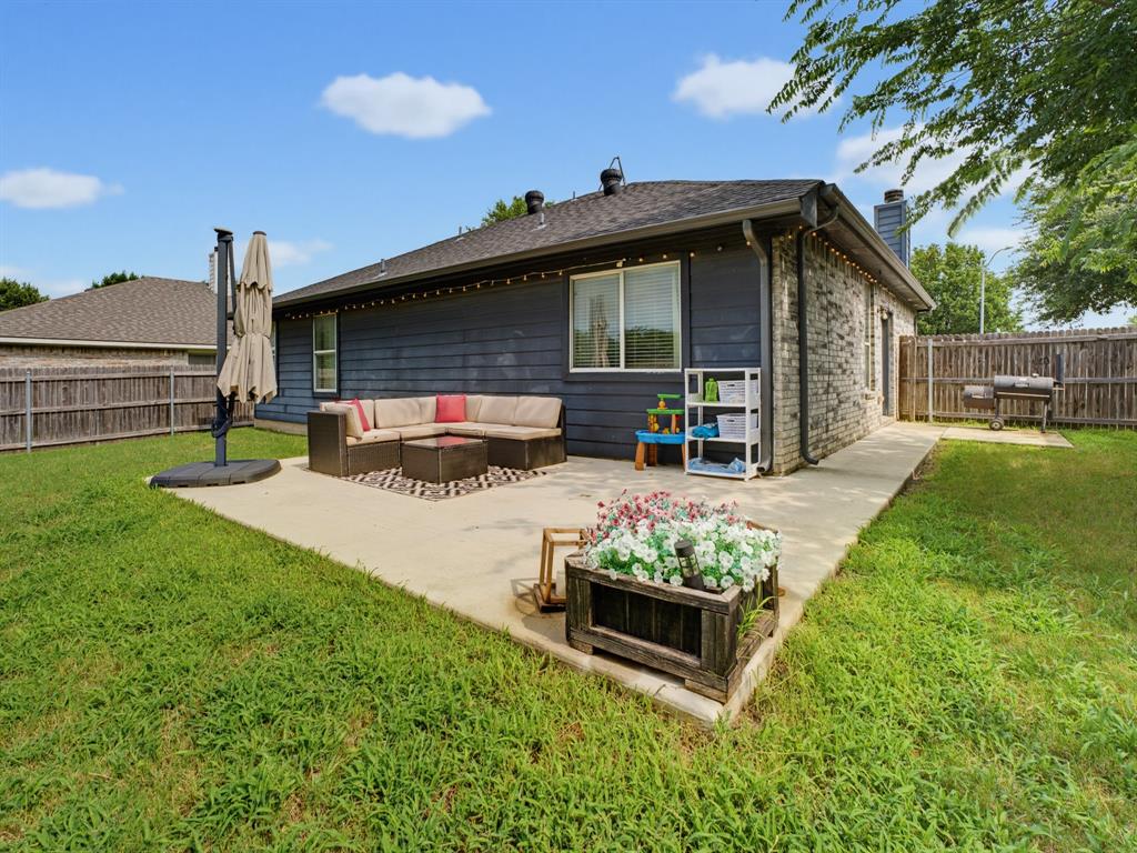 600 Stirling Road Rhome, TX 76078 - Photo 32 of 38 Expansive backyard featuring a concrete patio, dark gray siding, light gray brick exterior, a wooden privacy fence, and a concrete pathway