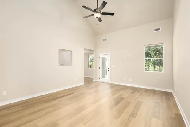 an empty room with wooden floor ceiling fan and windows