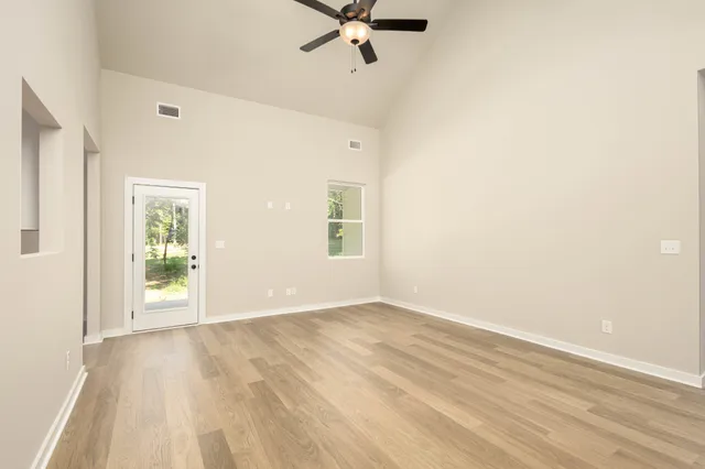 an empty room with wooden floor chandelier fan and windows