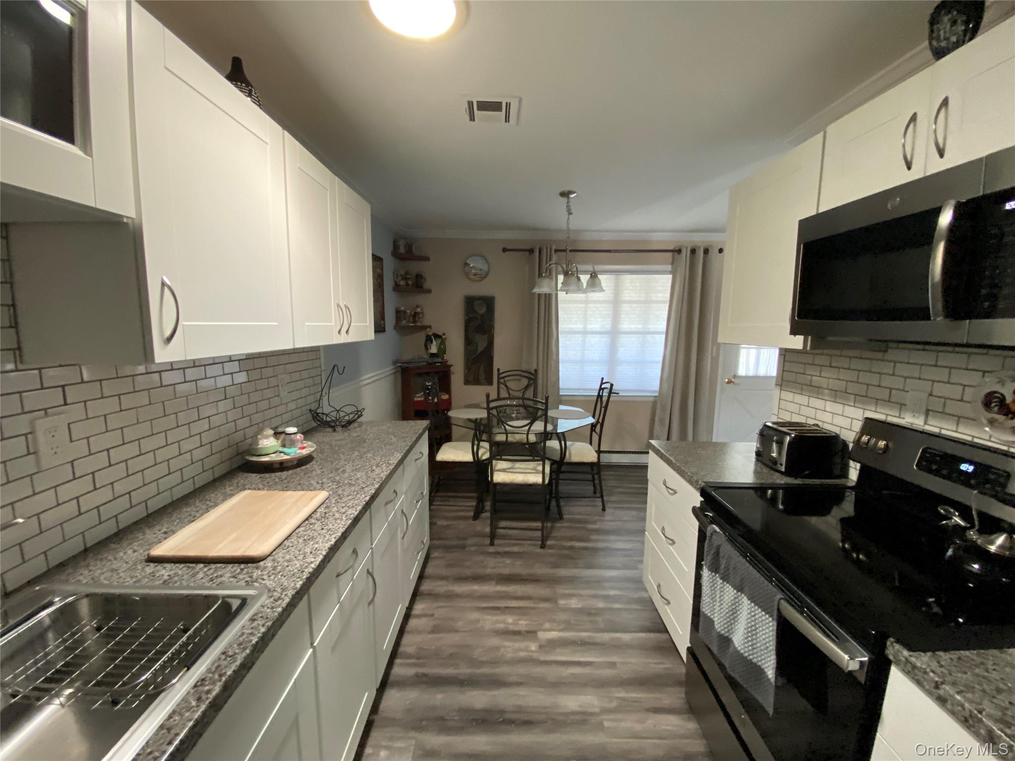 274 Berwick Court, Unit A Ridge, NY 11961 - Photo 15 of 31 Kitchen featuring black range with electric stovetop, decorative backsplash, stainless steel microwave, white cabinetry, and crown molding