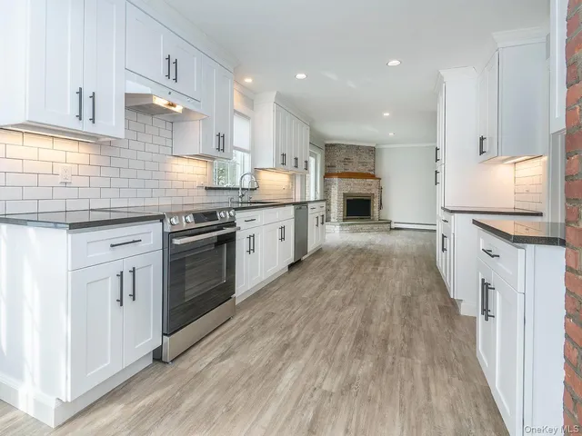 a large kitchen with granite countertop a stove top oven a sink dishwasher and a fireplace with wooden floor