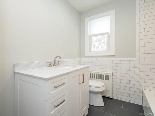 a bathroom with a granite countertop toilet a sink a mirror and a window