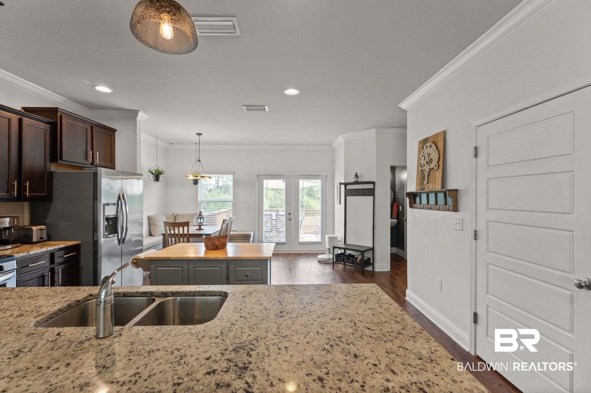 12711 Chickadee Lane Daphne, AL 36527 - Photo 12 of 39 Kitchen with ornamental molding, dark wood-type flooring, light stone countertops, dark brown cabinetry, and stainless steel fridge with ice dispenser
