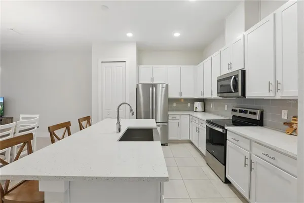 a kitchen with stainless steel appliances a stove top oven a sink a refrigerator with white cabinets and wooden floor