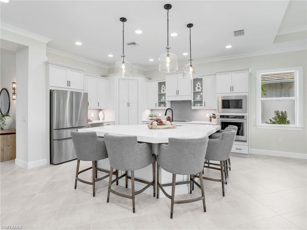8850 Calypso Court Naples, FL 34113 - Photo 10 of 49 a kitchen with stainless steel appliances kitchen island granite countertop a dining table chairs and a refrigerator