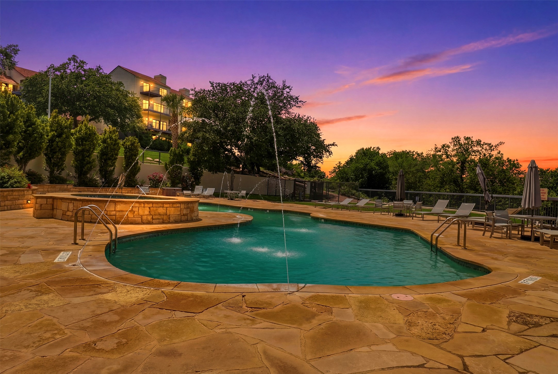 2918 Ranch Road 620, Unit 265 Austin, TX 78734 - Photo 37 of 40 An inviting pool area with multiple water features glows under a vibrant sunset, ideal for evening relaxation.