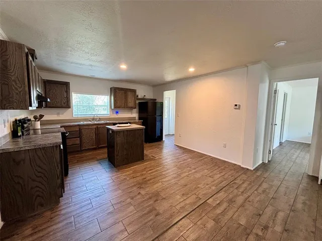 a kitchen with stainless steel appliances granite countertop wooden cabinets a refrigerator a stove a sink and a oven with wooden floors