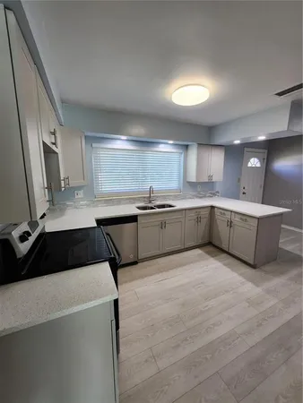 a large white kitchen with a sink and dishwasher a stove top oven with wooden floor