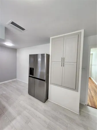 a view of an empty room with wooden floor and a kitchen