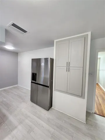 a view of an empty room with wooden floor and a kitchen