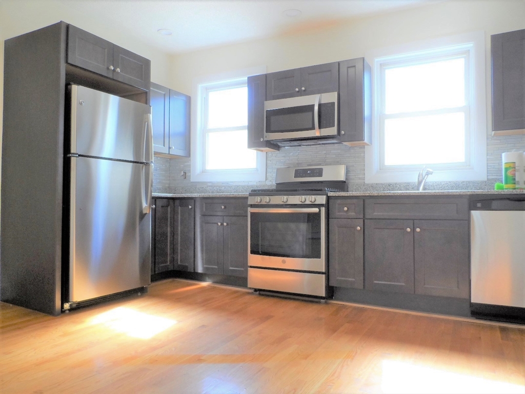 a kitchen with stainless steel appliances granite countertop a refrigerator a stove a sink and dishwasher with wooden floor