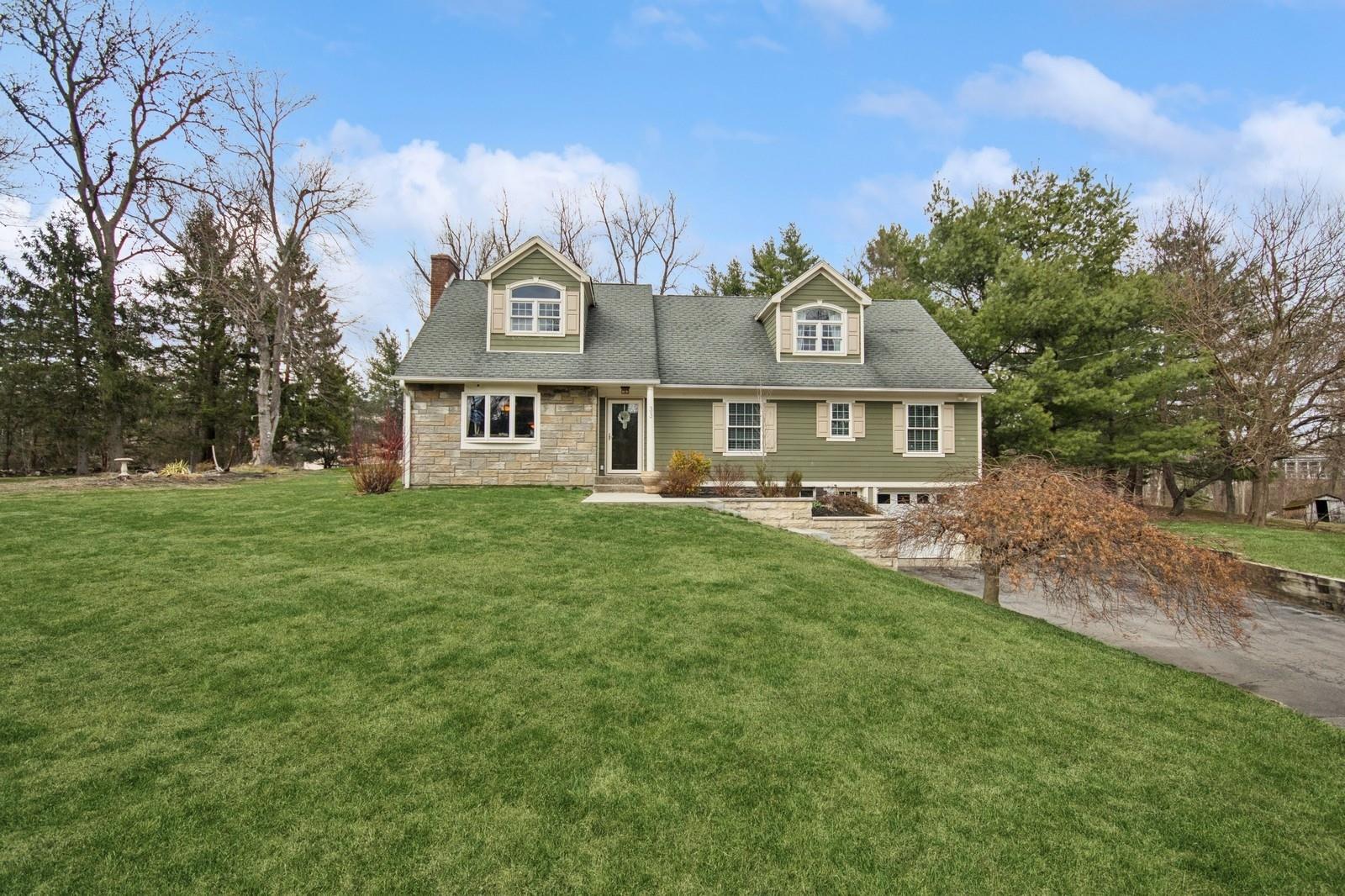 Cape cod house featuring stone siding, a chimney, a shingled roof, and a front yard