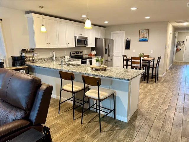 a kitchen with stainless steel appliances granite countertop a stove top oven a sink a dining table and chairs with wooden floor