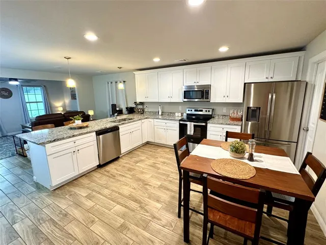 a kitchen with stainless steel appliances granite countertop a stove top oven a refrigerator a sink and a dining table with wooden floor