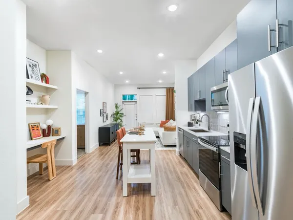 a kitchen with stainless steel appliances a refrigerator a stove top oven a sink dishwasher and white cabinets with wooden floor