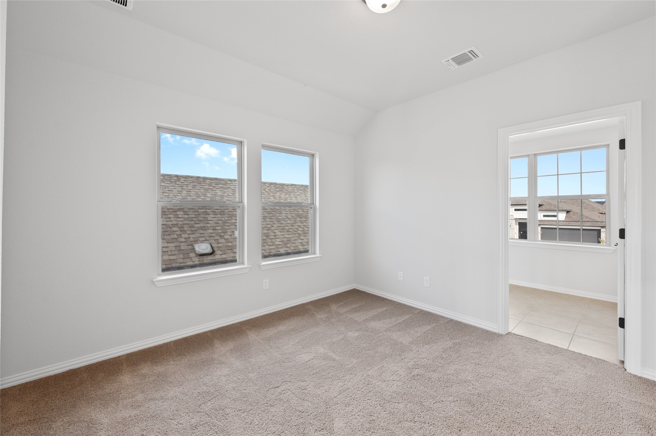303 Fawn Riv Run Kyle, TX 78640 - Photo 20 of 32 Carpeted room with white walls, two double-hung windows, and a doorway opening to a tiled area