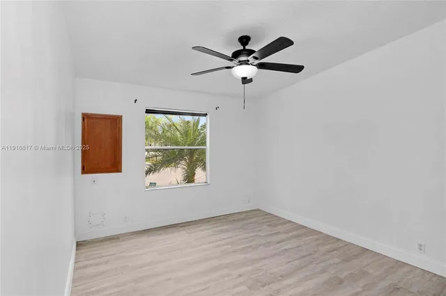an empty room with wooden floor fan and windows