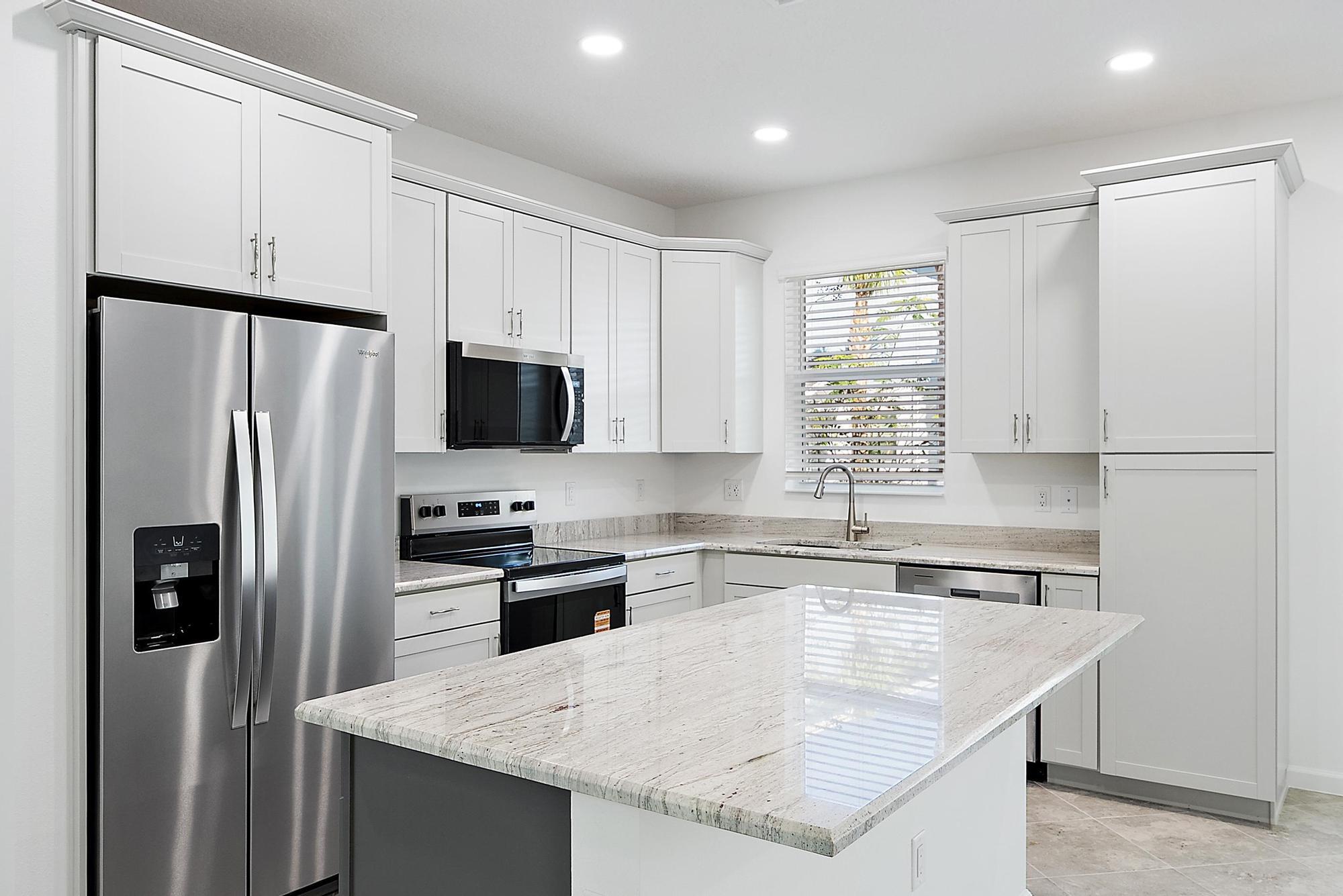 a kitchen with granite countertop a refrigerator a sink a stove a microwave and island