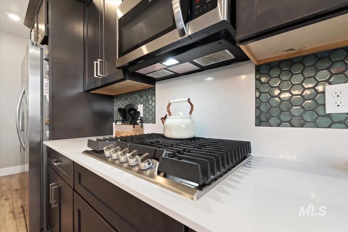 815 Knowledge Street Middleton, ID 83644 - Photo 14 of 49 Kitchen featuring a built-in gas range, stainless steel microwave, white countertops, dark wood-finish cabinetry, and a hexagonal tile backsplash