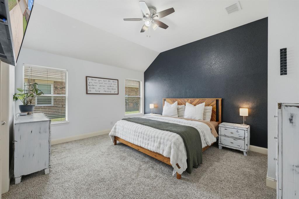 14152 Rodeo Daze Drive Fort Worth, TX 76052 - Photo 14 of 20 Vaulted ceiling bedroom featuring a dark accent wall, two windows with blinds, a ceiling fan, and grey carpet flooring