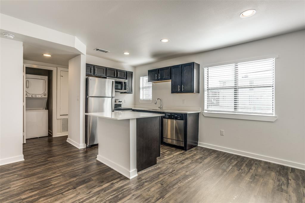 2106 Bennett Avenue, Unit 209 Dallas, TX 75206 - Photo 13 of 22 Open-concept kitchen featuring dark cabinetry, stainless steel appliances, a central island with a white countertop, and wood-finish flooring
