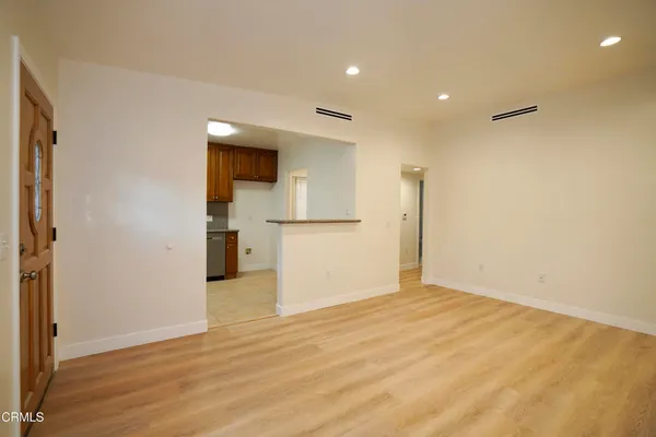 an empty room with wooden floor and a kitchen