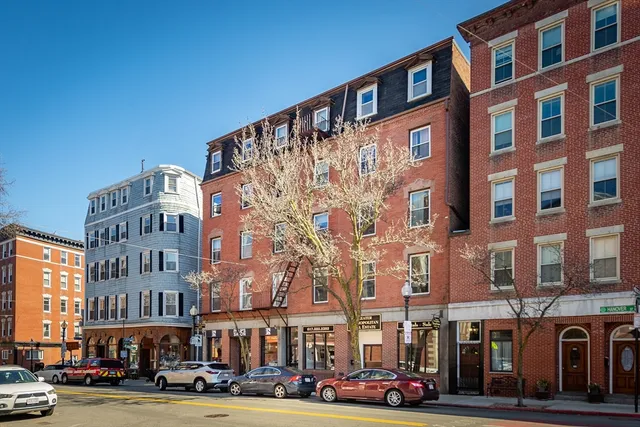 a front view of a building with lot of cars and trees