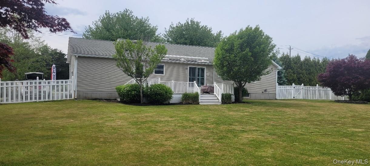 312 Riley Avenue Calverton, NY 11933 - Photo 21 of 30 Expansive rear lawn featuring a white Vinyl fence, mature trees, and a ground-level deck with white vinyl fencing and sliding glass door access