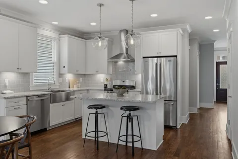 a kitchen with stainless steel appliances granite countertop a refrigerator a sink dishwasher a stove and white cabinets with wooden floor