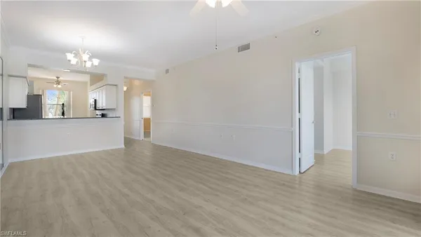 an empty room with wooden floor and kitchen view