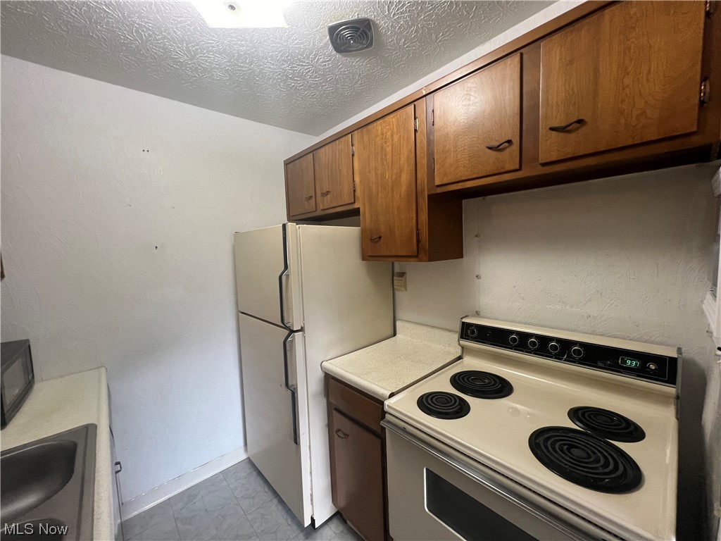 5651 Broadview Road, Unit C 07 Cleveland, OH 44134 - Photo 7 of 15 Kitchen with sink, a textured ceiling, white refrigerator, light tile floors, and range with electric stovetop