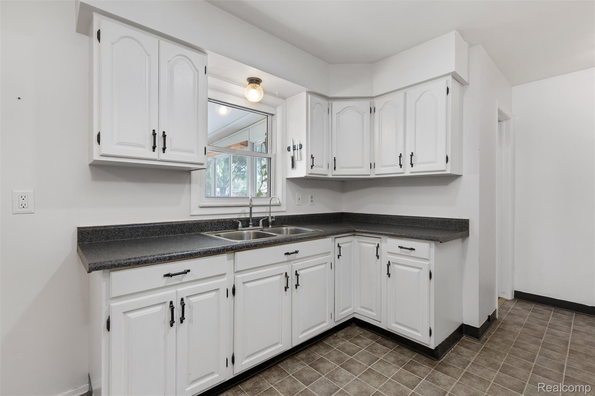 4497 Reid Road Swartz Creek, MI 48473 - Photo 5 of 31 Kitchen featuring white cabinetry, dark countertops, a double basin stainless steel sink, and tiled flooring
