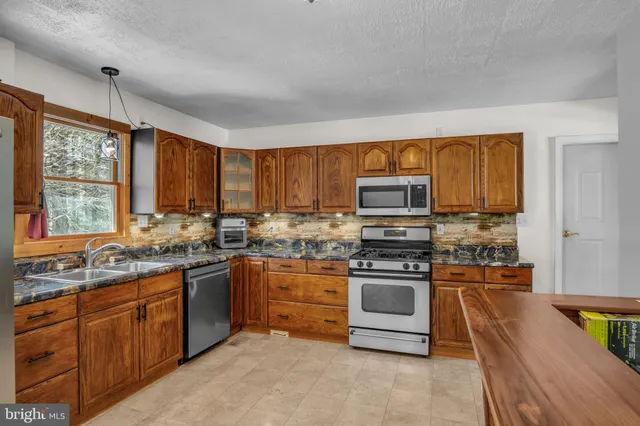 a kitchen with stainless steel appliances granite countertop wooden cabinets a stove a sink and dishwasher with wooden floor