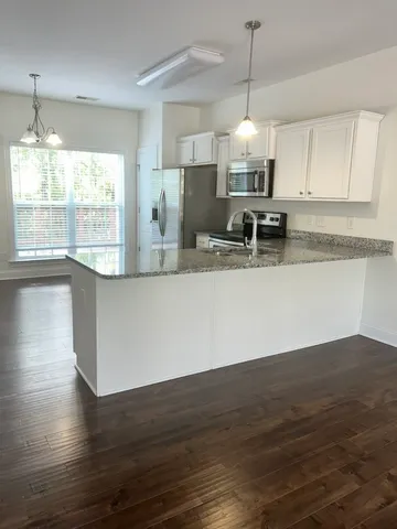 a large kitchen with granite countertop a stove a sink a window and wooden floor