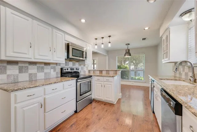 a kitchen with granite countertop cabinets stainless steel appliances a sink and a wooden floor