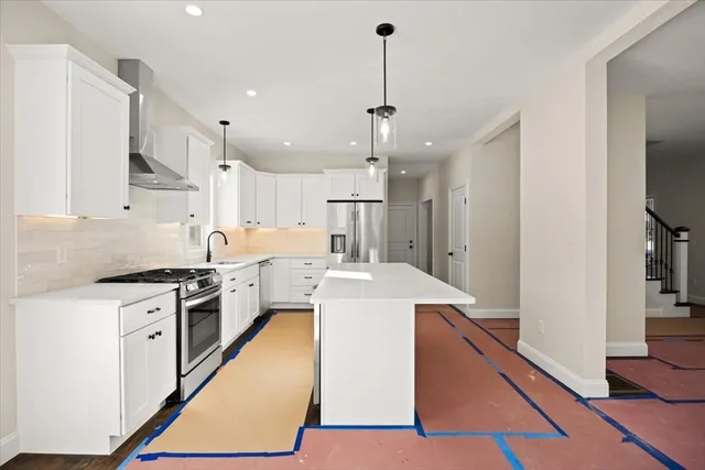 a large kitchen with stainless steel appliances granite countertop a stove a sink dishwasher a refrigerator and white cabinets with wooden floor