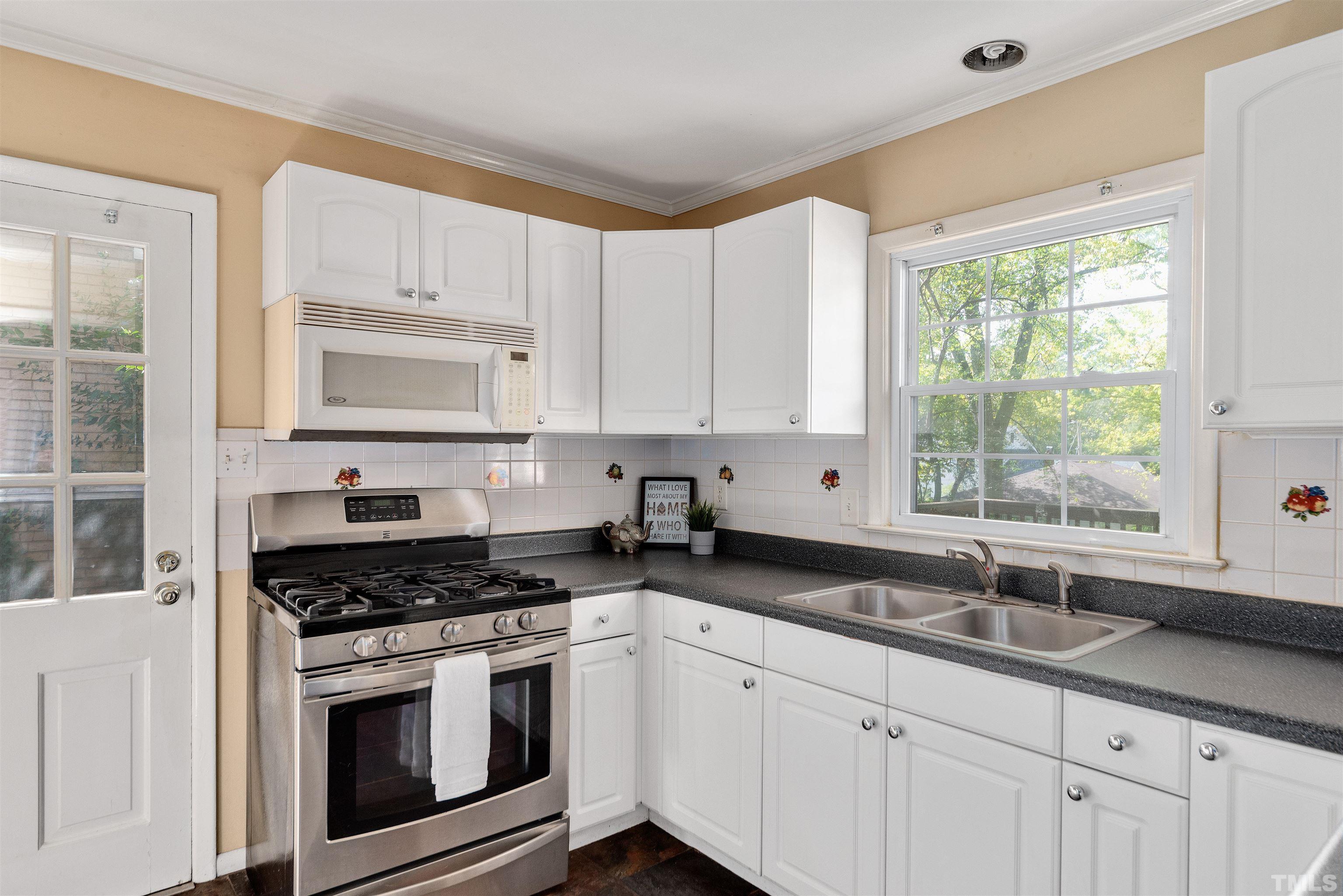 711 Latta Street Raleigh, NC 27607 - Photo 9 of 30 a kitchen with granite countertop white cabinets a sink a window and stainless steel appliances