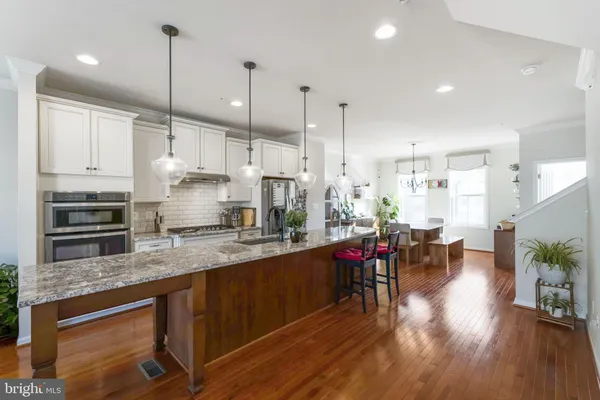 a kitchen with stainless steel appliances granite countertop a stove sink refrigerator dining table and chairs with wooden floor