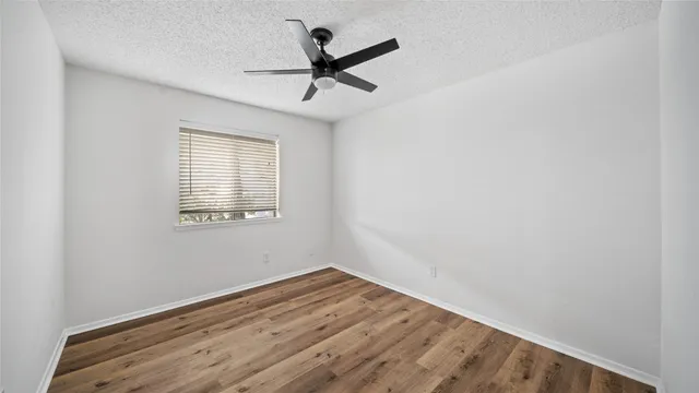an empty room with wooden floor ceiling fan and windows