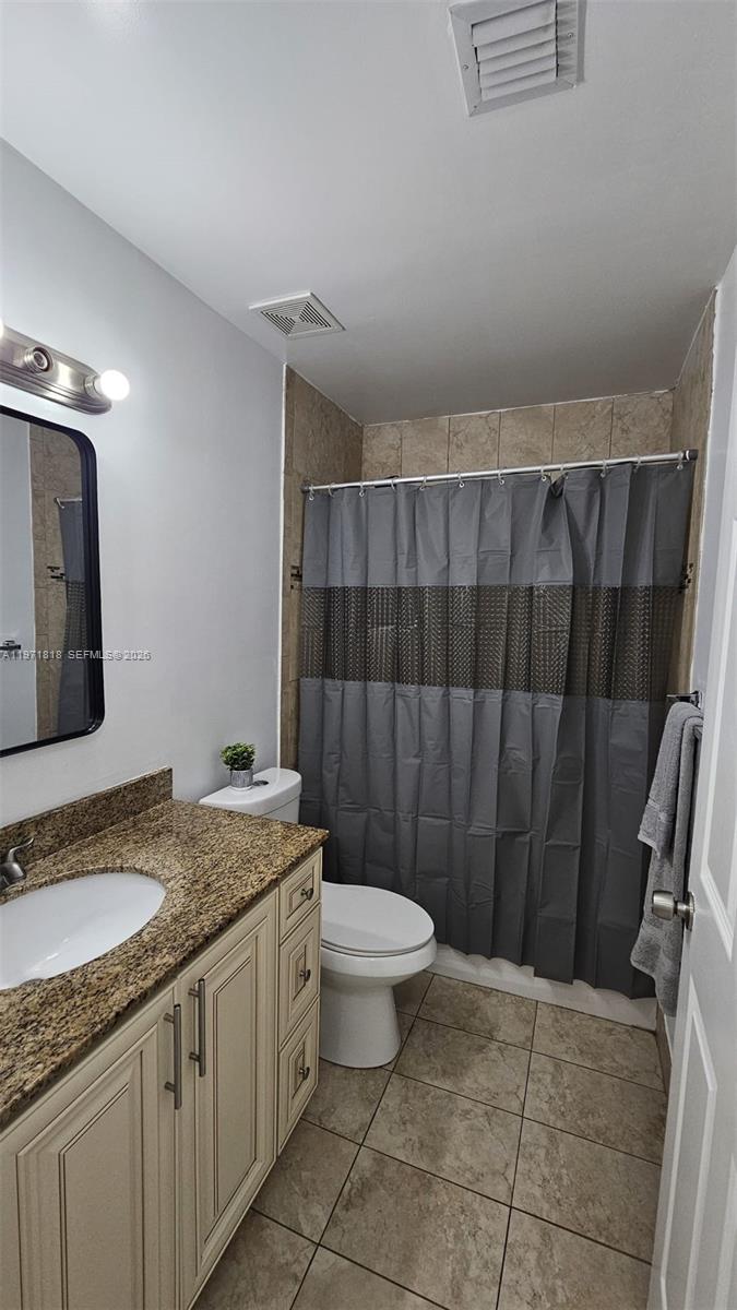 535 Northwest 19th Street, Unit 369 Miami, FL 33136 - Photo 7 of 26 a bathroom with a granite countertop sink a toilet a mirror and shower curtain