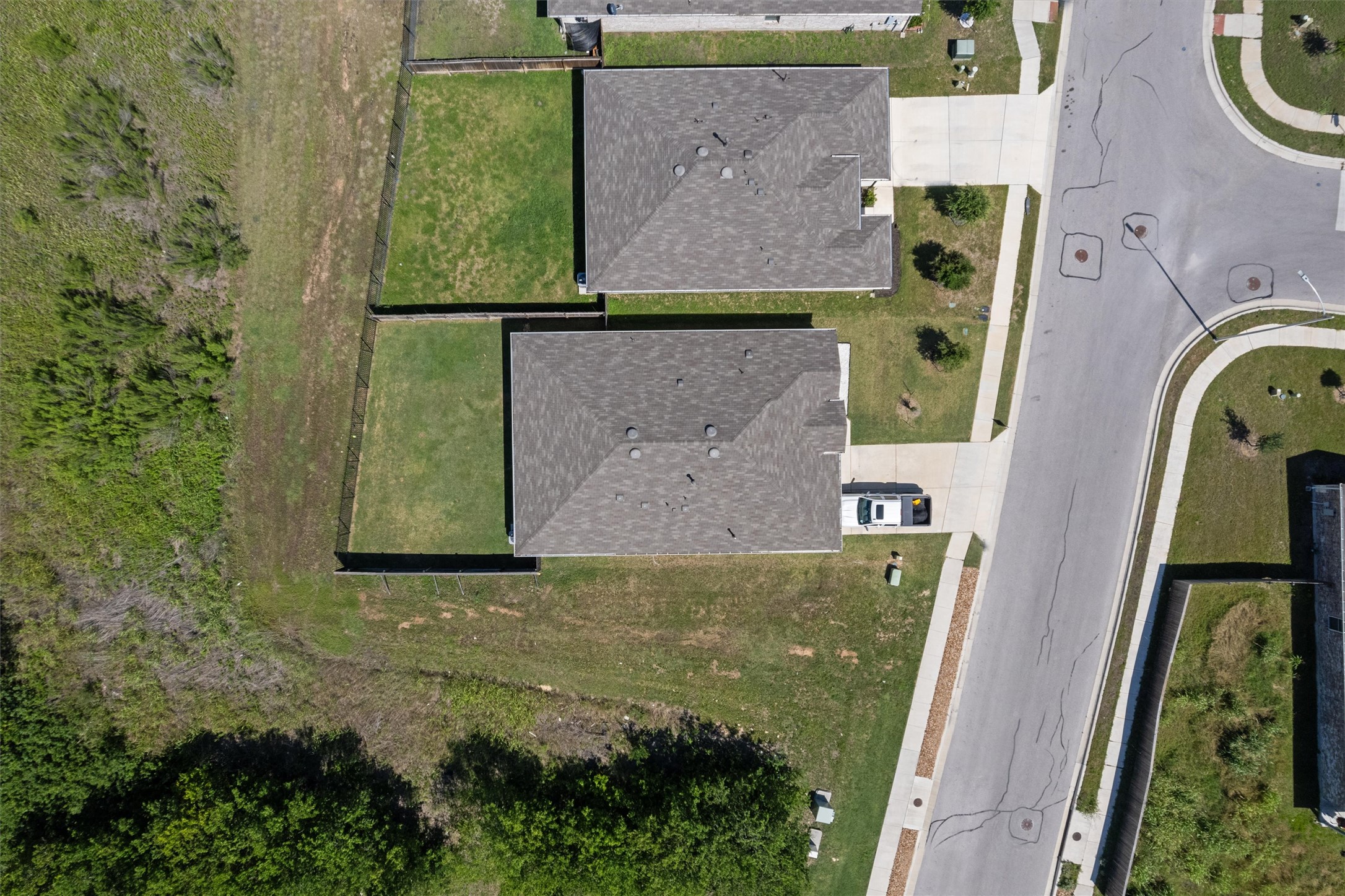 19912 Abigail Fillmore Road Manor, TX 78653 - Photo 28 of 31 An aerial perspective reveals two homes with fenced backyards, bordering a natural landscape and residential street.