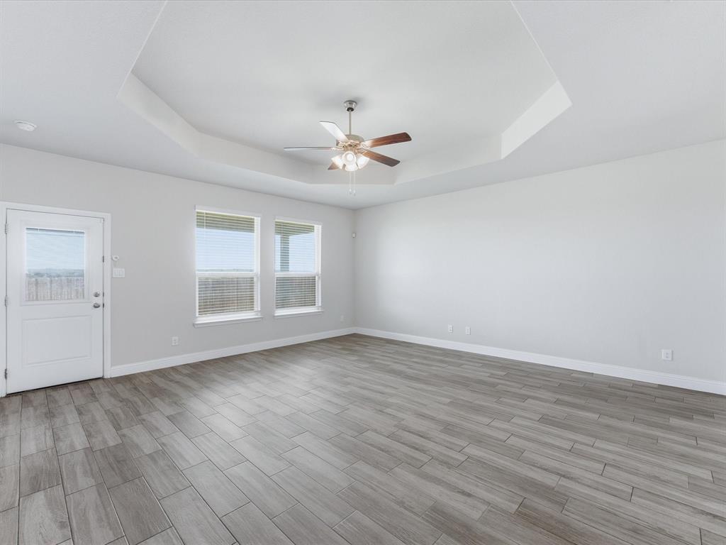 1121 Knightsbridge Road Argyle, TX 76226 - Photo 20 of 39 Living room featuring a tray ceiling with a ceiling fan, a white exterior door with a clear glass insert, two windows with blinds, and wood-finish flooring