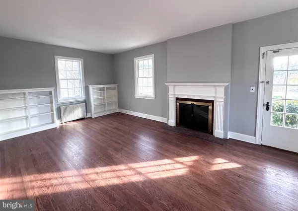 an empty room with wooden floor fireplace and windows